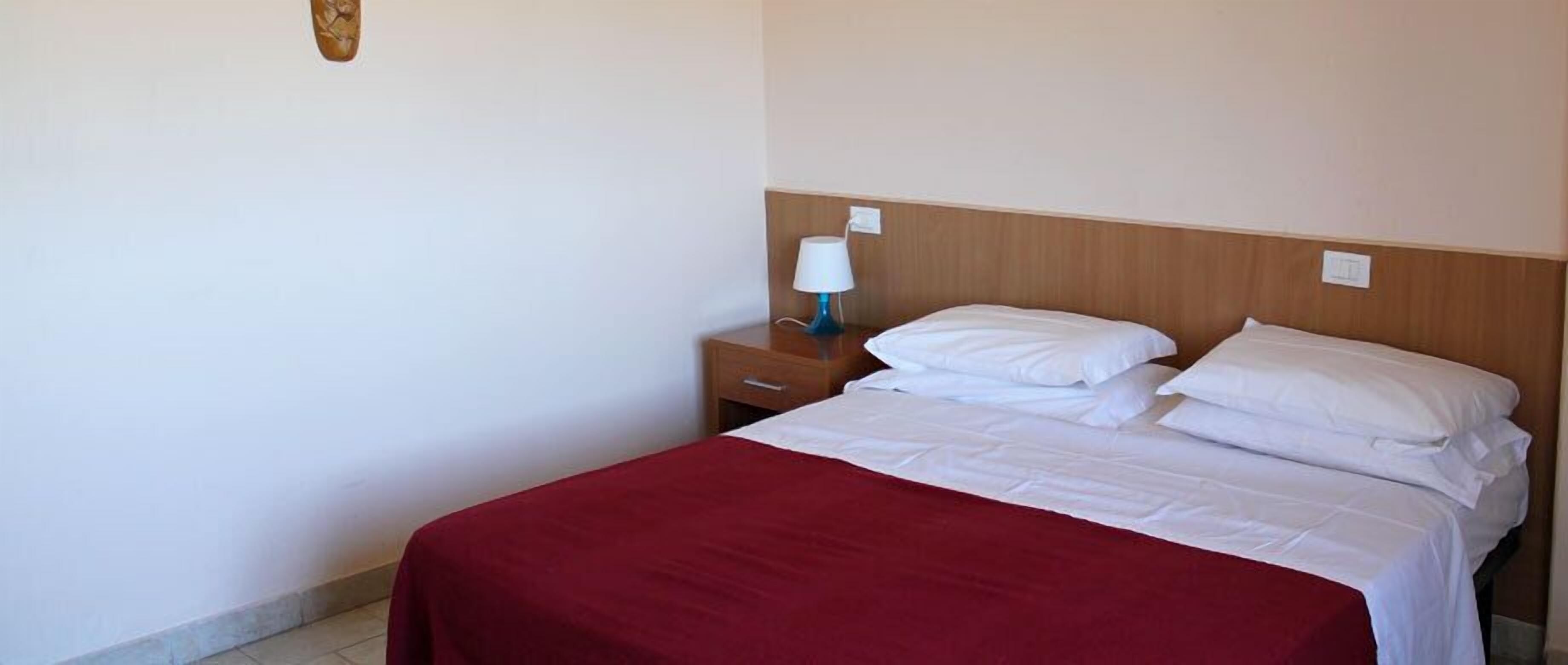 Ein Hotelzimmer mit Bett, Nachttisch, Lampe und Wandleuchte.
