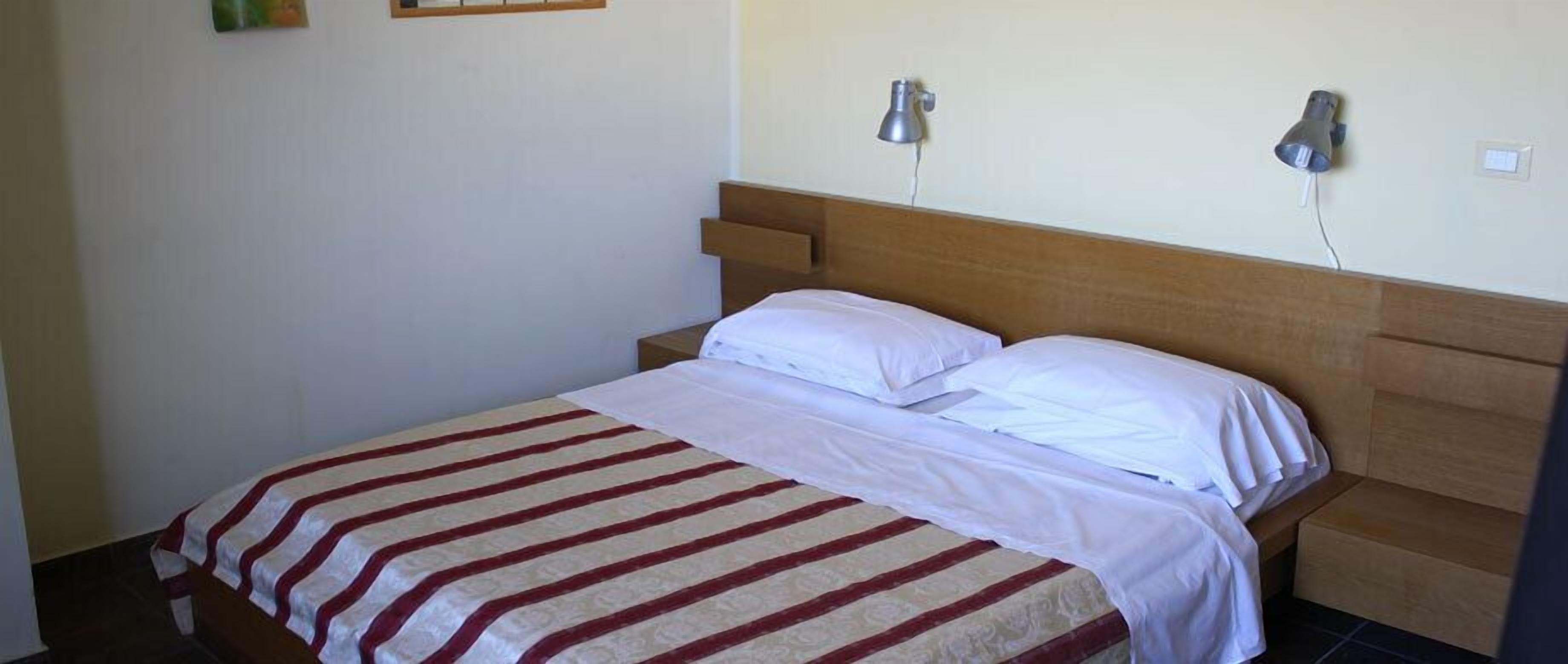 A neatly made bed with a striped bedspread, a wooden headboard, and two wall-mounted lamps.