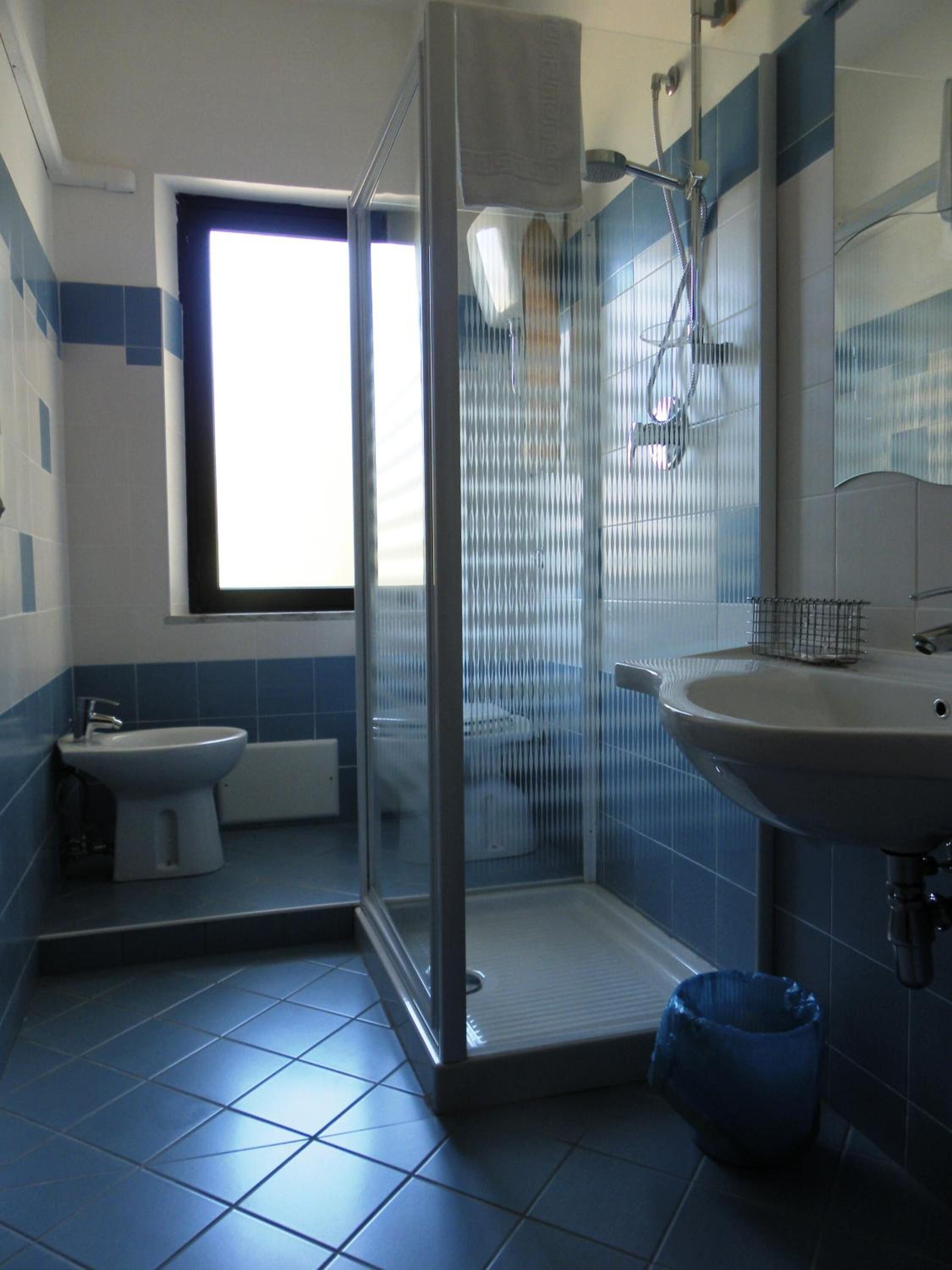 Un baño con ducha de vidrio, lavamanos, inodoro y ventana.