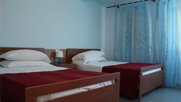 Una camera d'albergo con due letti in legno, biancheria da letto bianca, un comodino con una lampada e una finestra con tende blu.