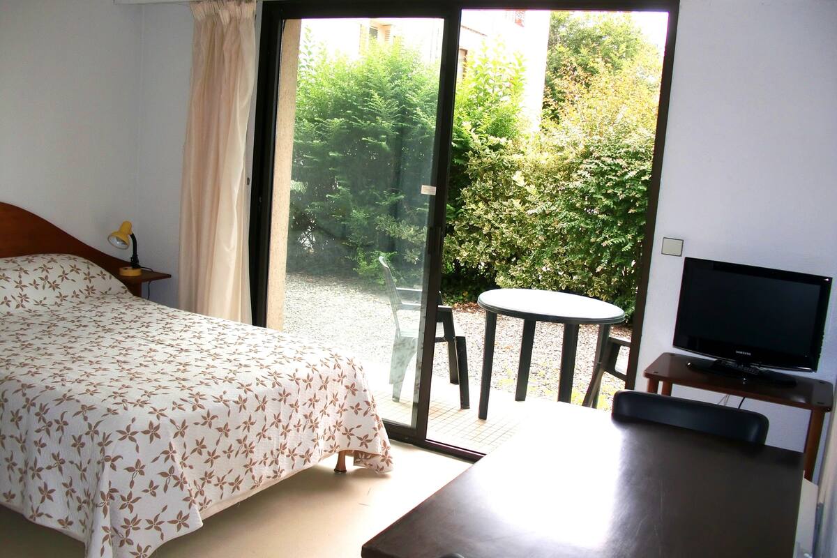Ein Hotelzimmer mit Bett, Fernseher, Tisch und Blick auf Grünfläche.