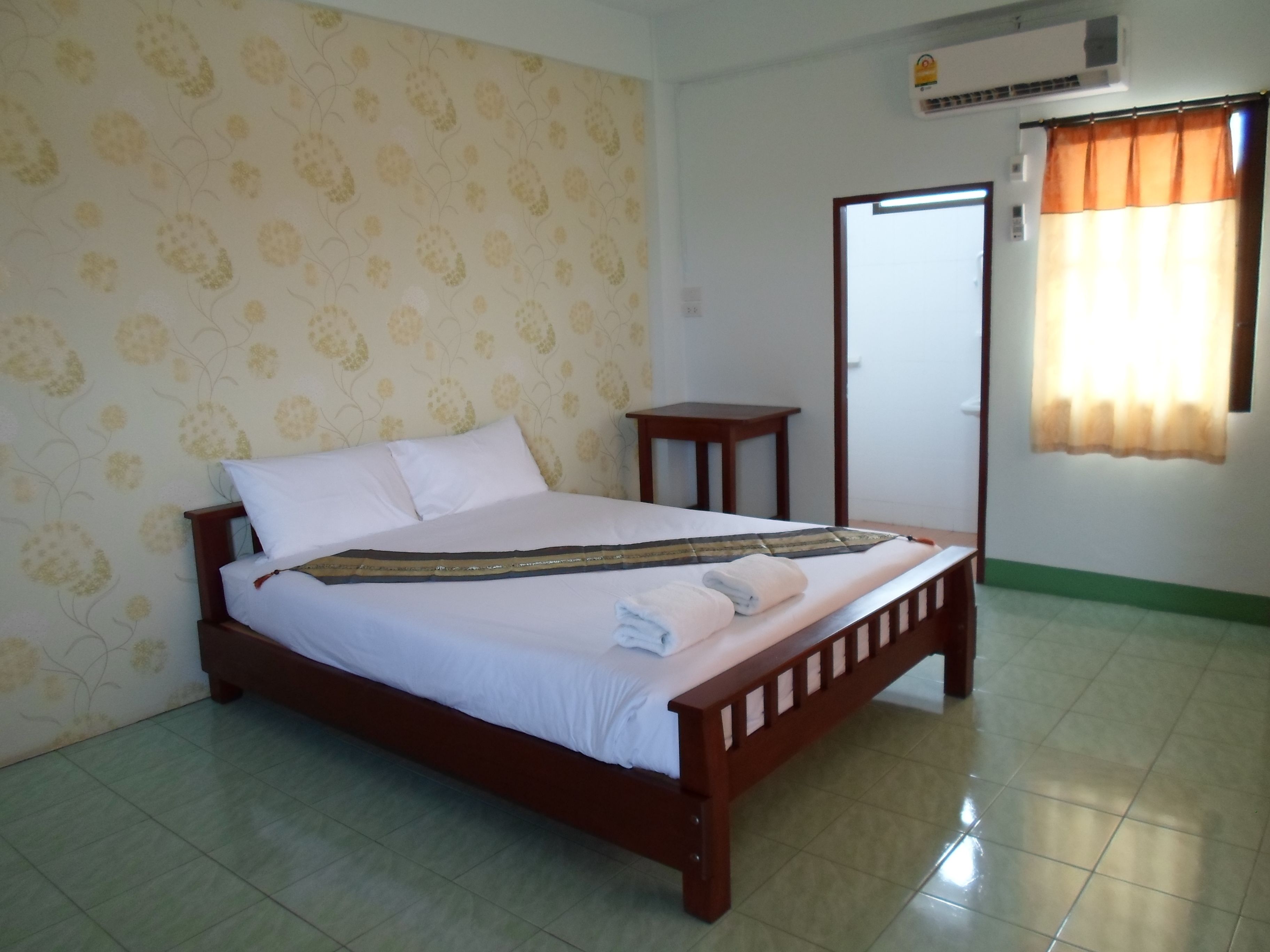 A neatly made bed with white linens and a decorative pillow, a small wooden nightstand, and a window with curtains.