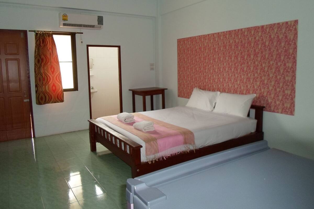 Een slaapkamer met een bed, een klein tafeltje, een spiegel en een airconditioning.