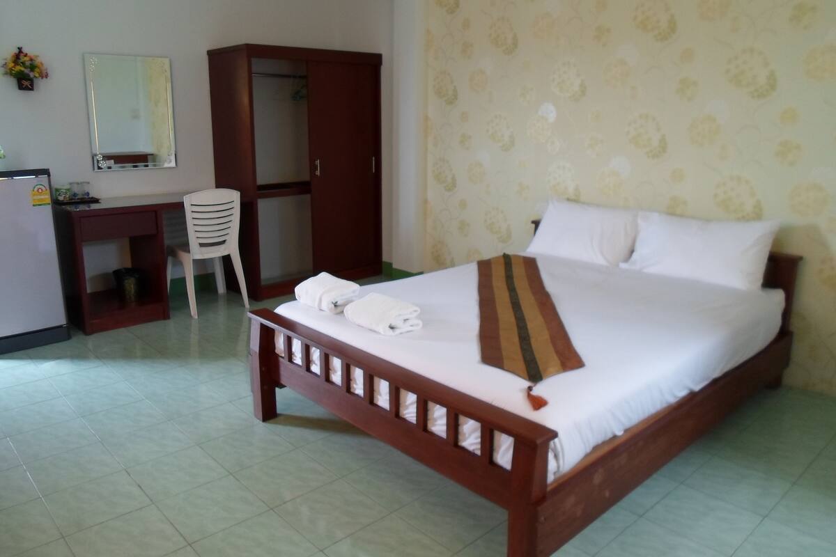 Een hotelkamer met een houten bed, een bureau, een stoel, een kledingkast en een spiegel.
