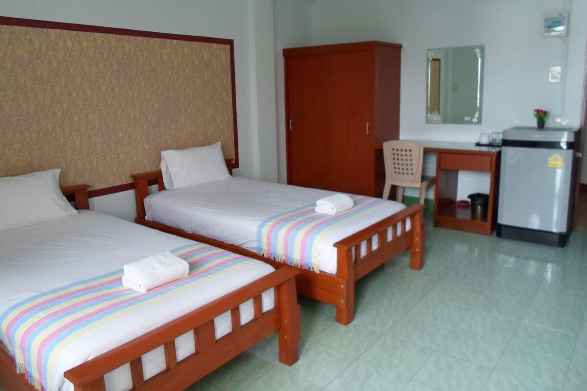 Een hotelkamer met twee enkele bedden, een bureau, een kleine koelkast en een spiegel.