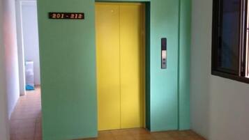 A hallway with a green wall, a yellow elevator, and a sign with numbers.