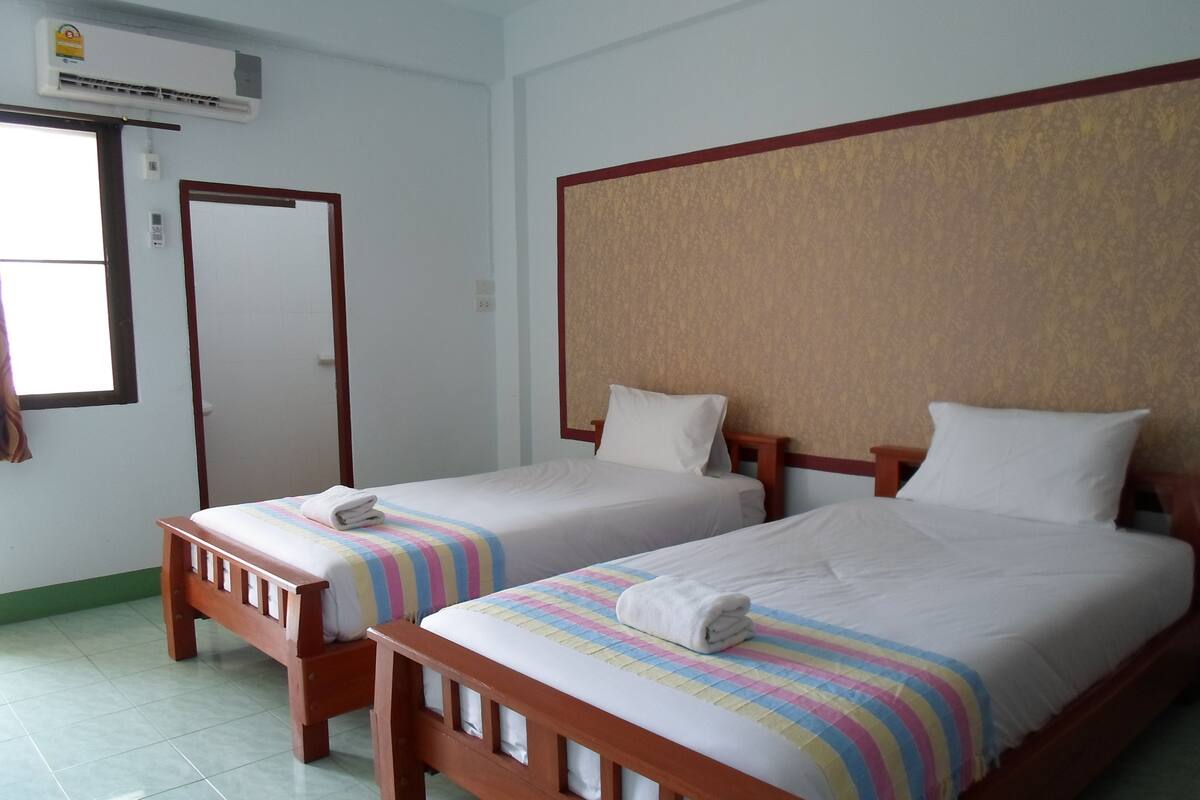 Een hotelkamer met twee enkele bedden, een houten hoofdbord, een gestreepte deken en een betegelde vloer.