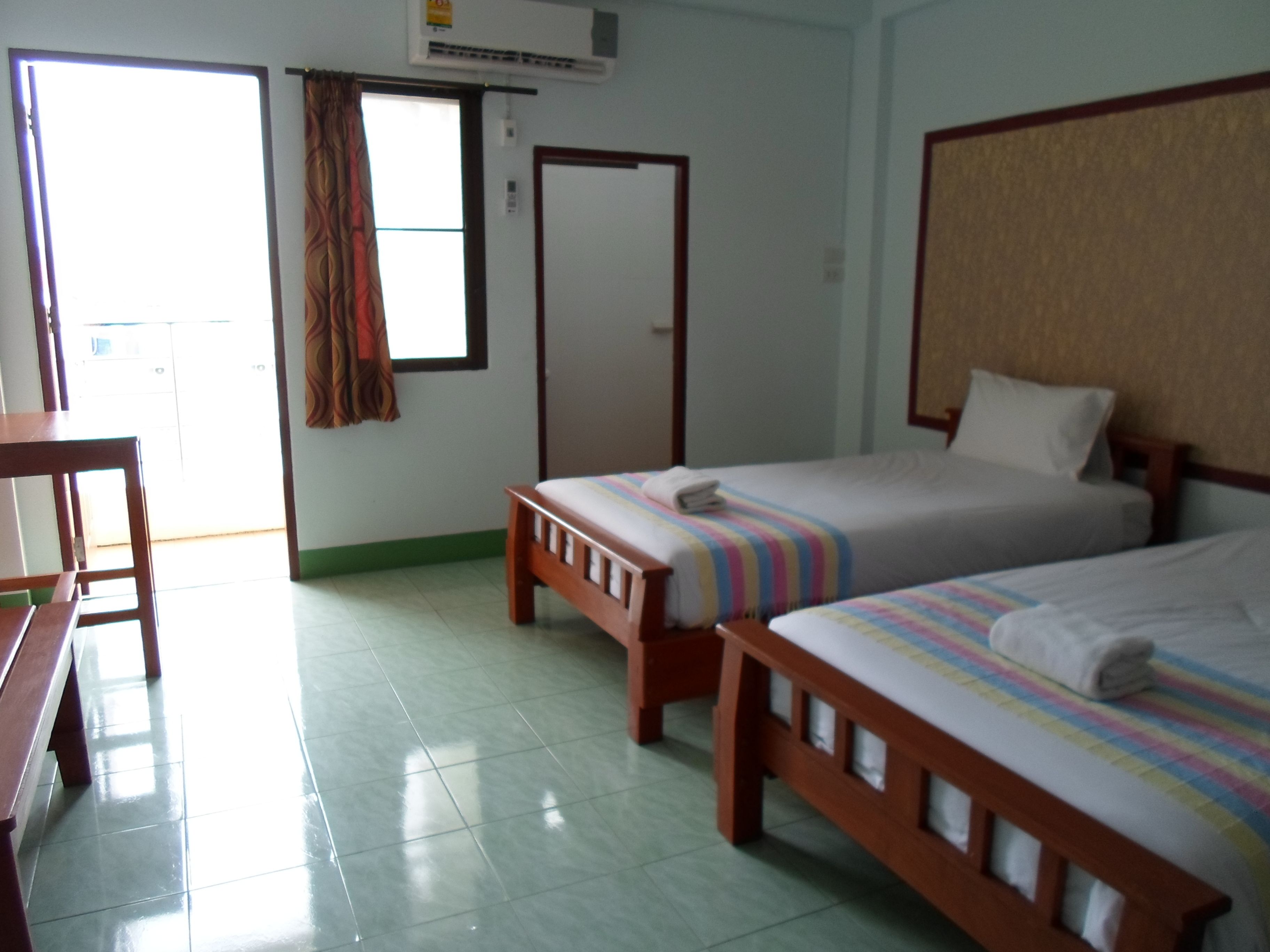 Habitación de hotel con dos camas individuales, un escritorio de madera, una silla y una ventana con cortinas.