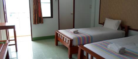 Habitación de hotel con dos camas individuales, un escritorio de madera, una silla y una ventana con cortinas.