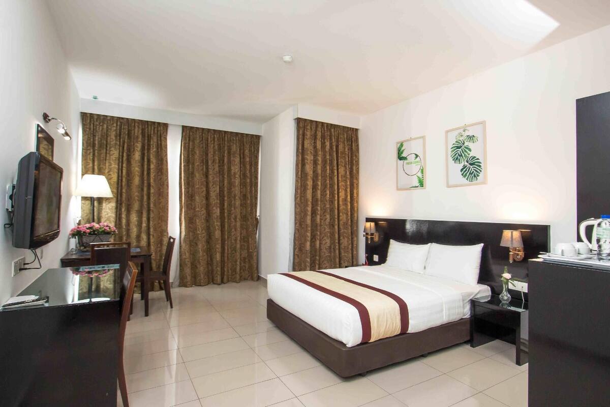 A hotel room with a bed, a desk, a chair, a television, a nightstand, and a coffee machine.
