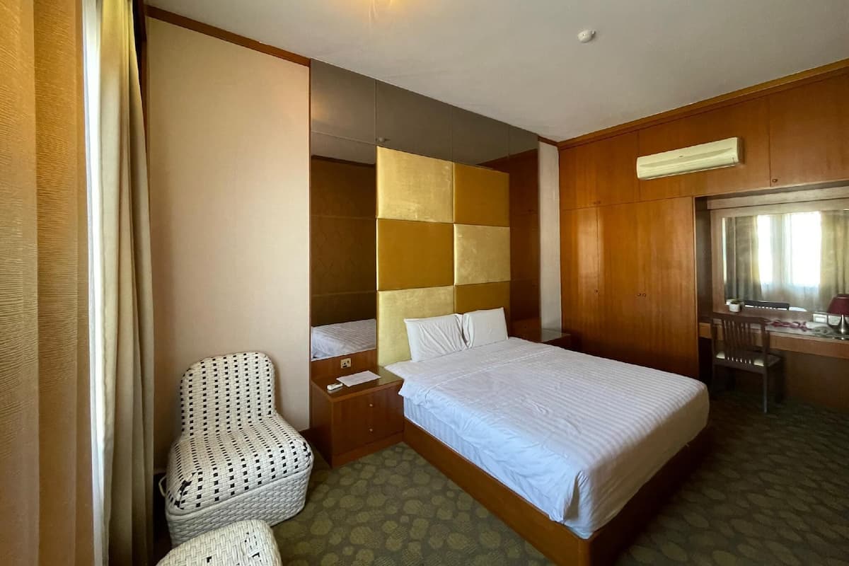 A hotel room with a bed, a chair, a desk, and a mirror.