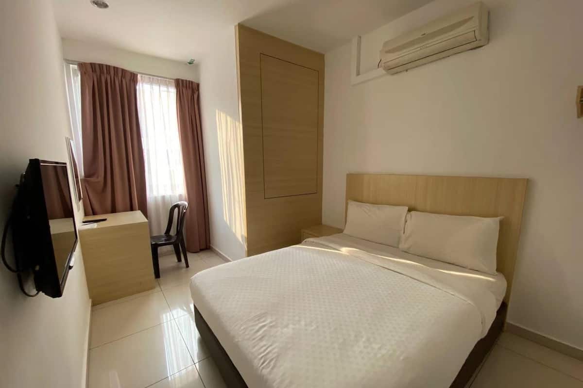 A hotel room with a bed, a desk, a chair, an air conditioning unit, and a window with curtains.