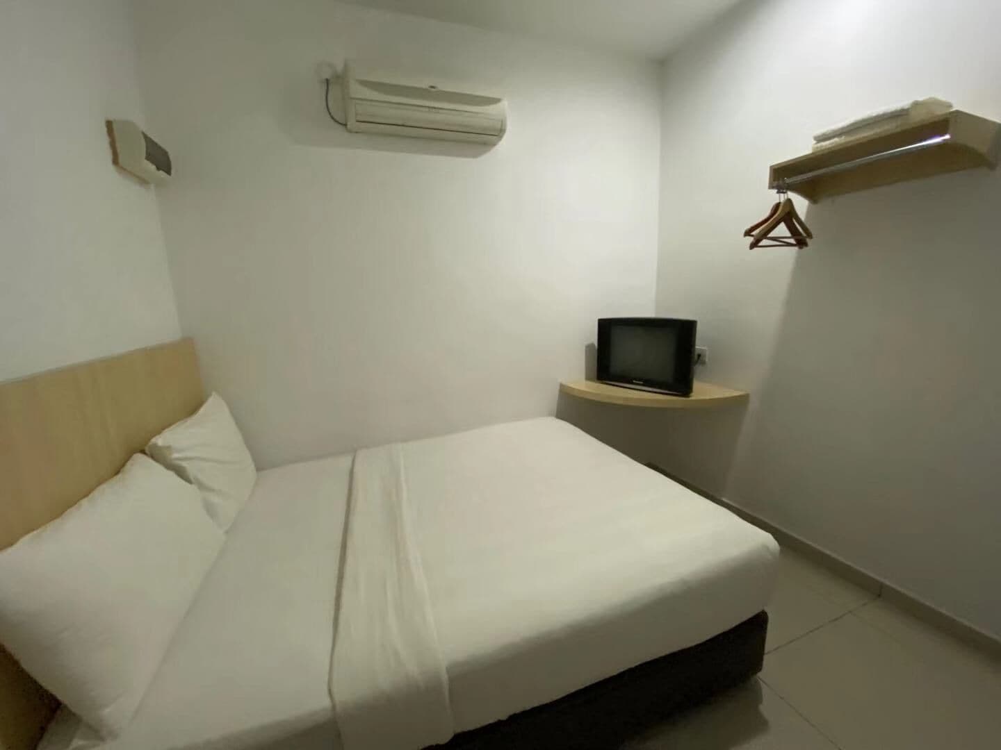 Une chambre d’hôtel avec un lit, un téléviseur posé sur une petite table et un appareil de climatisation fixé au mur.
