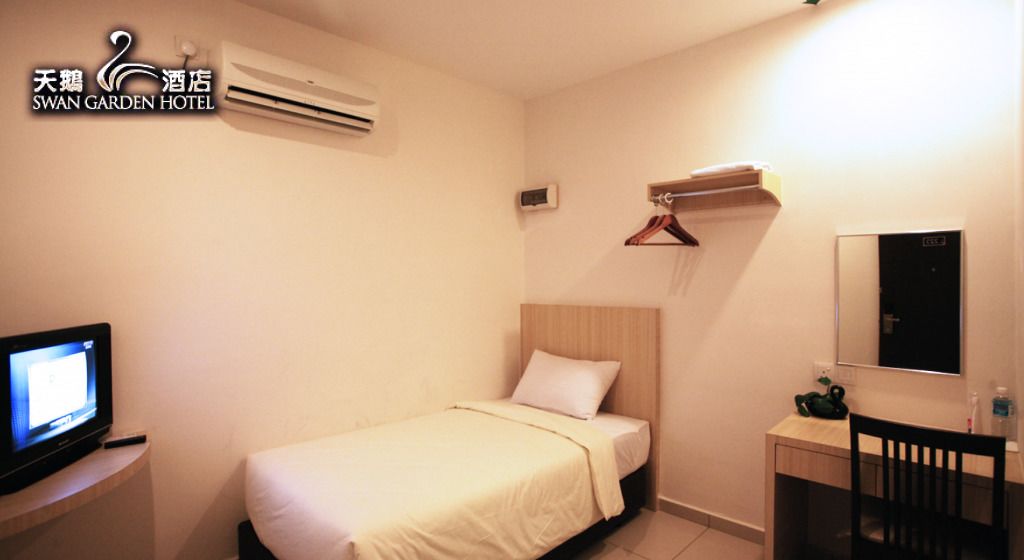 A hotel room with a bed, a TV, a desk, a chair, a mirror, and a coat rack.