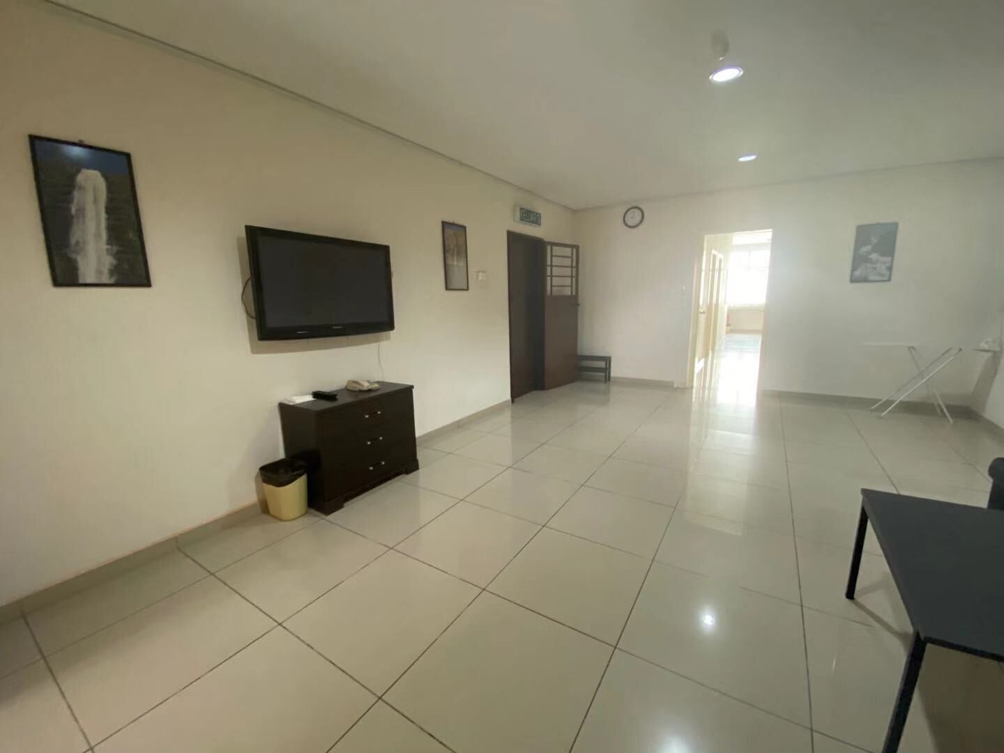 A spacious room with a flat-screen TV mounted on the wall, a dark wooden cabinet, and a tiled floor.