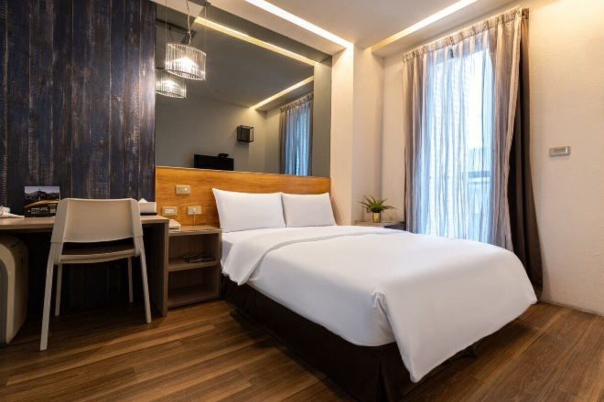 Habitación de hotel con cama de madera, un escritorio con silla, una mesita y una planta.