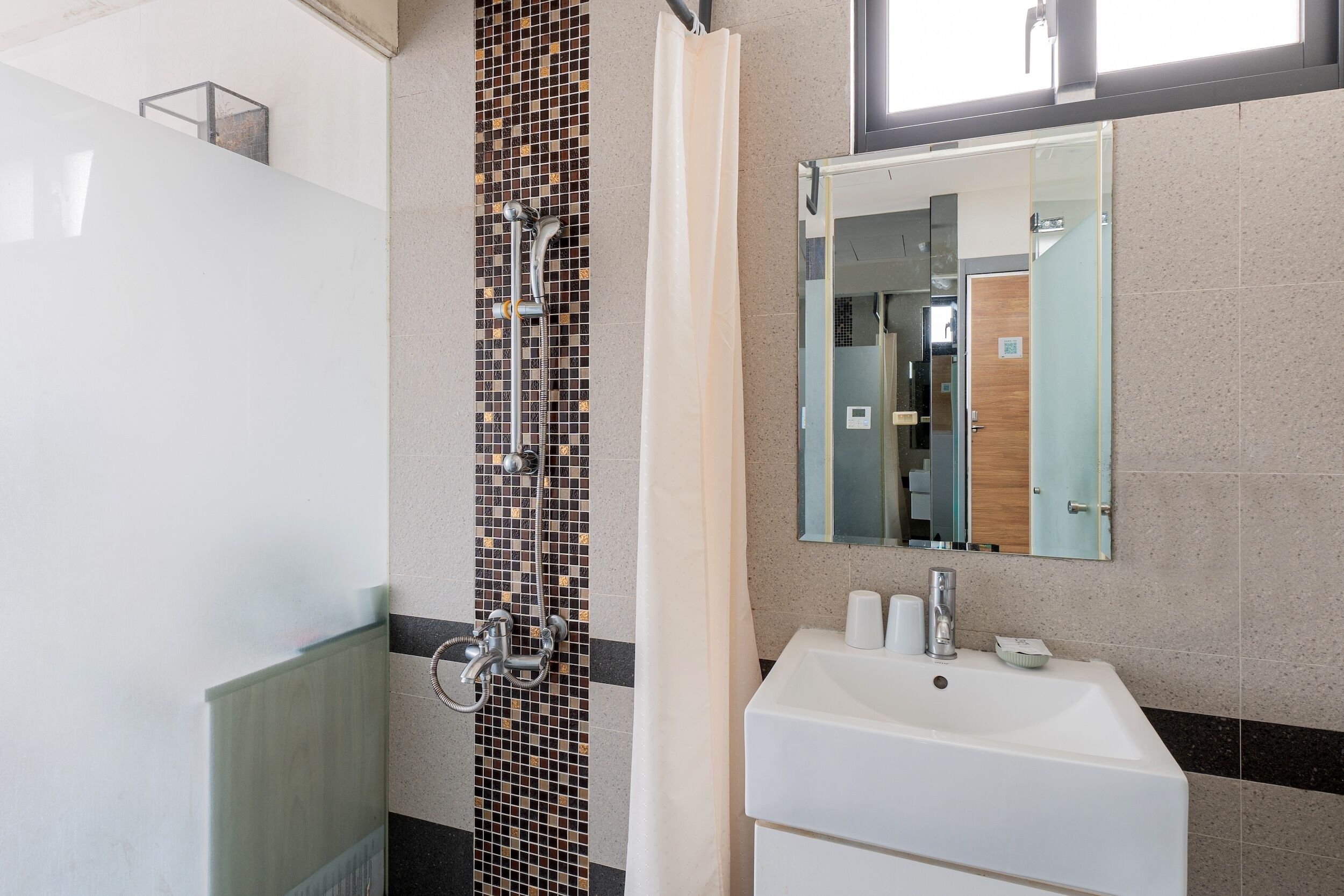 Ein Badezimmer mit einem weißen Waschbecken, einem Spiegel und einer Dusche mit gefliesten Wänden.
