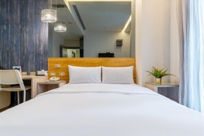 Habitación de hotel con una cama grande, un escritorio con silla, un teléfono y una planta en maceta.