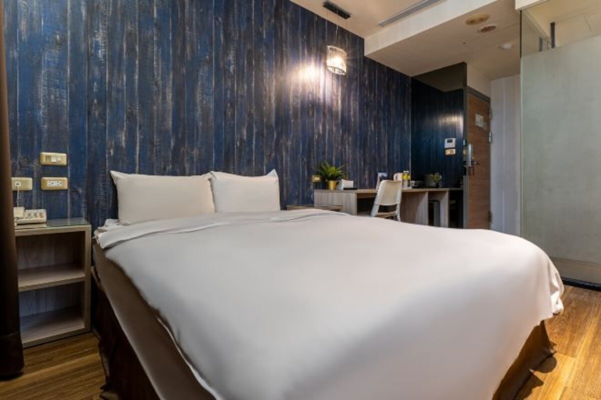 Una habitación de hotel moderna con una cama grande, un panel de madera decorativo, un escritorio con una silla y una planta pequeña.