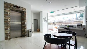 A modern hotel lobby with a stone-clad elevator, a reception desk, and a dining area with black chairs and a wooden table. - Hotel Zamburger Plaza Mahkota (Malacca City)