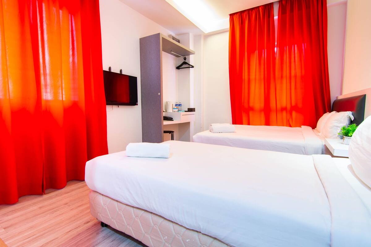 Ein Hotelzimmer mit zwei Betten, einem Kleiderschrank, einem Fernseher und einem kleinen Schreibtisch mit Pflanze.