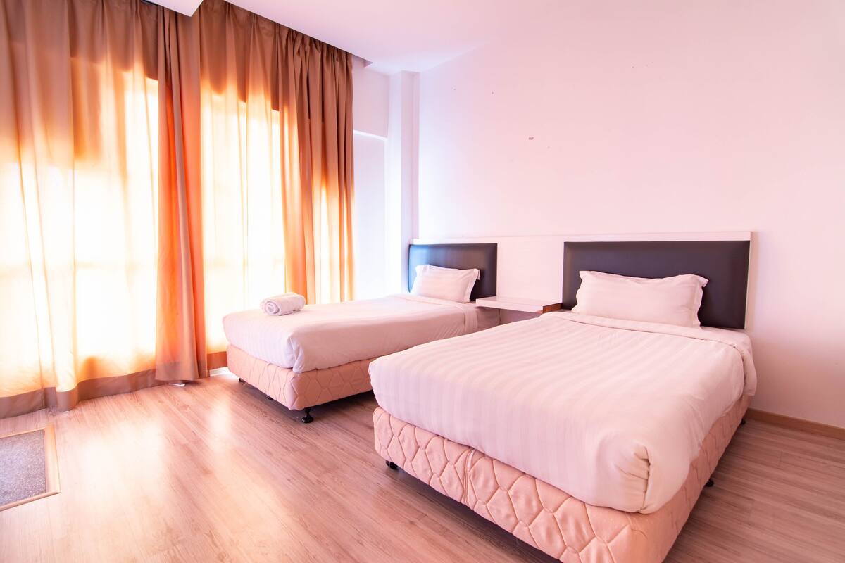 Ein Hotelzimmer mit zwei Betten, einem großen Fenster mit Vorhängen und einem Holzboden.
