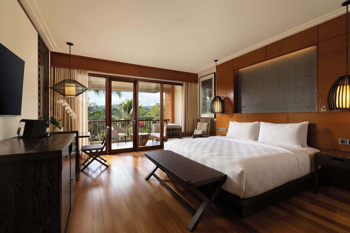 A spacious bedroom with a large bed, a desk, and a balcony with a view of the outdoors.