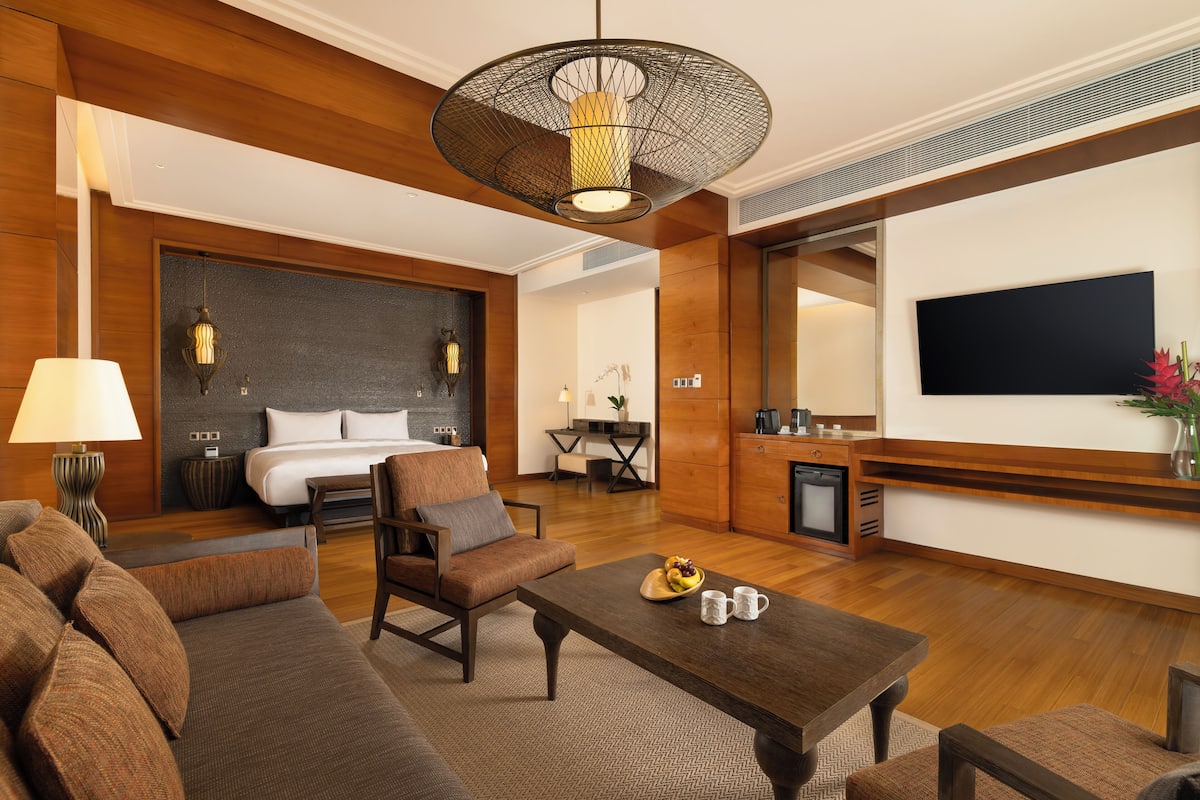 A modern hotel room with a large bed, a sofa, a coffee table, and a TV mounted on the wall.