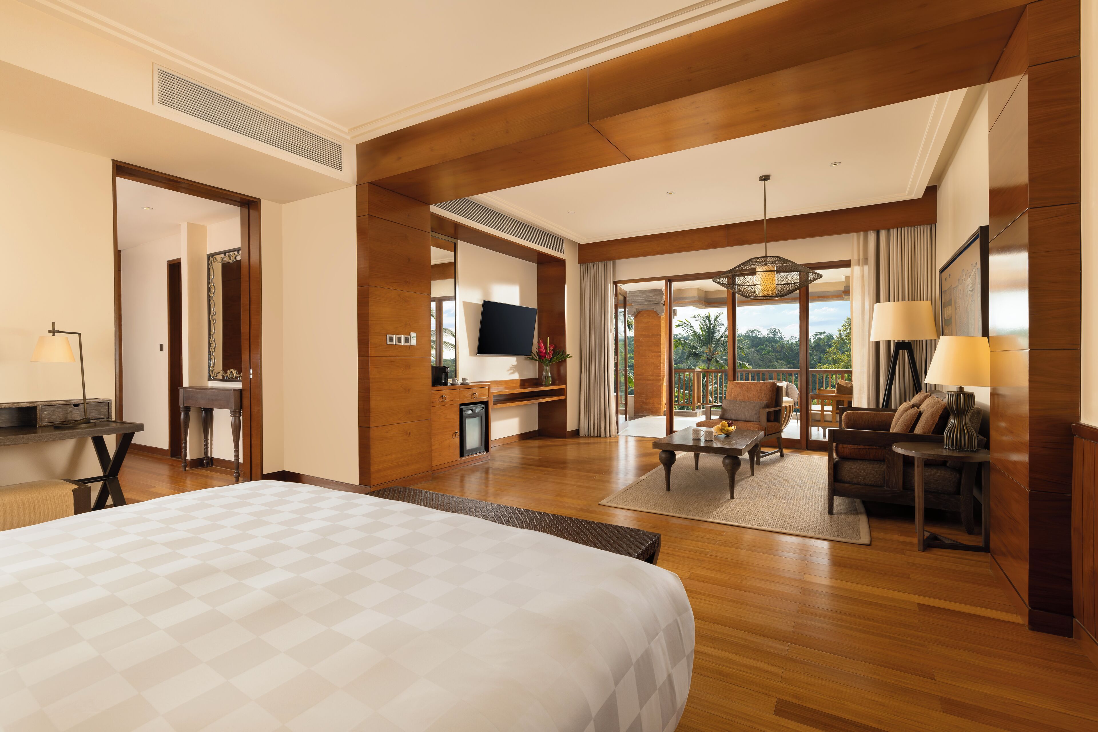 A spacious hotel room with a large bed, a desk, a television, and a balcony with a view.