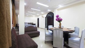 A dining area with a round table, chairs, and a vase of flowers. There are sofas and a door in the background. - Hotel Delhi Darbar (New Delhi)