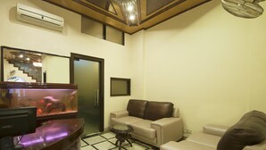 A living room with a fish tank, a sofa, a coffee table, and a TV. - Hotel Delhi Darbar (New Delhi)