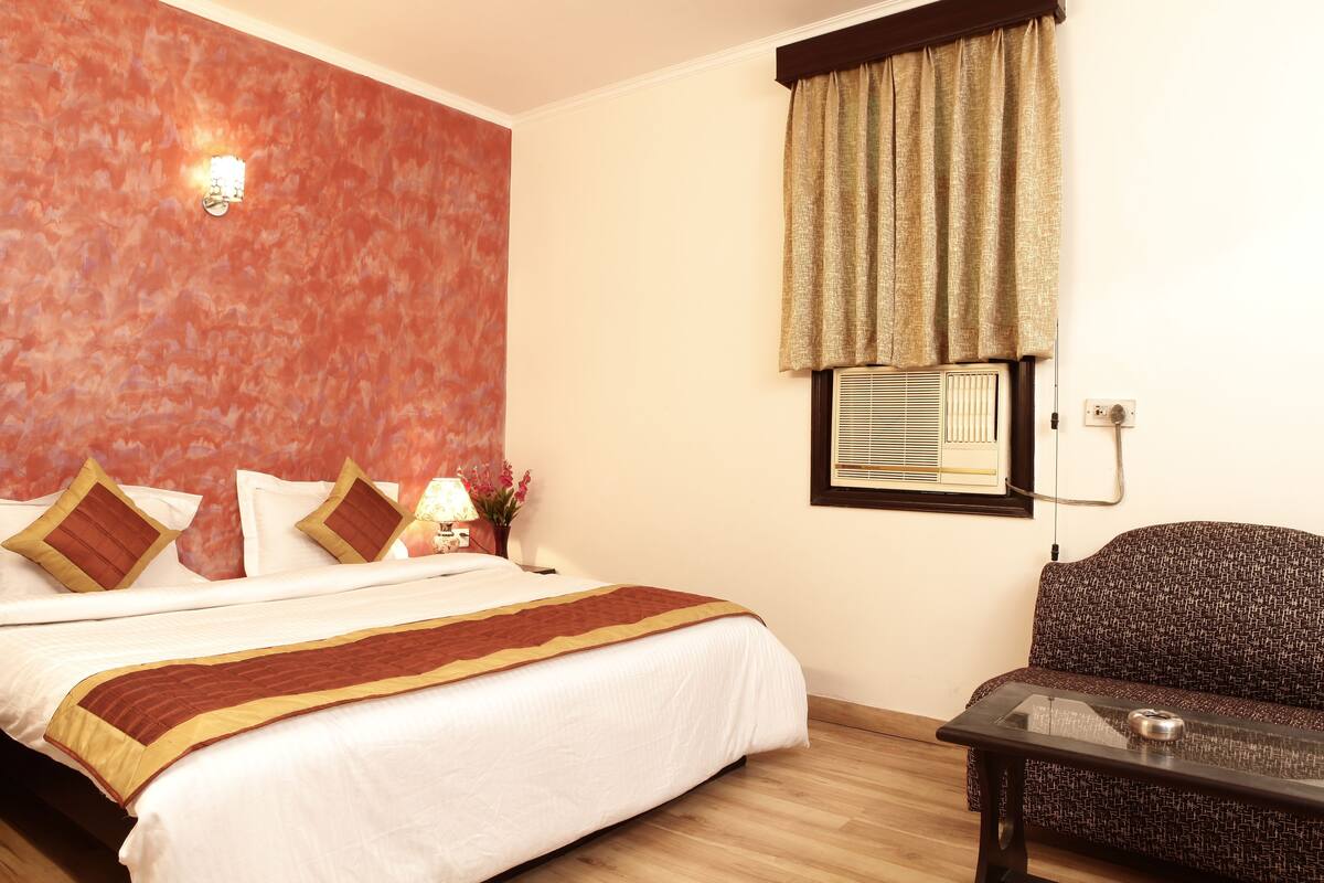 A hotel room with a bed, a sofa, a table, and a wall-mounted air conditioner.