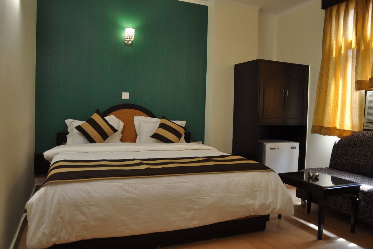 A hotel room with a bed, a desk, a wardrobe, and a window with curtains.