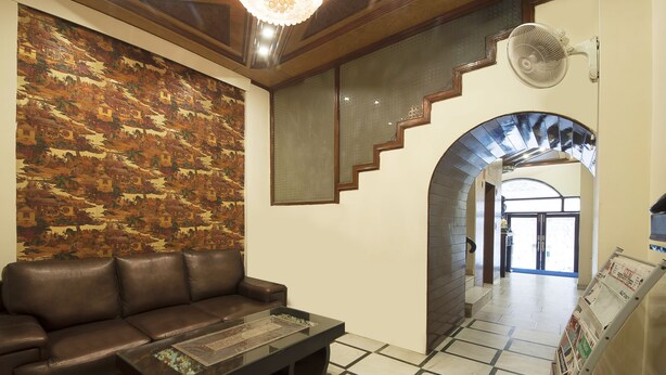 A lobby with a brown leather sofa, a coffee table, a patterned wall, a staircase, and a fan. - Hotel Delhi Darbar (New Delhi)