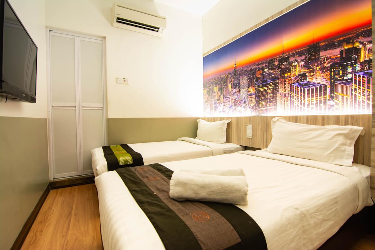 A hotel room with two beds, a cityscape mural on the wall, and a flat-screen TV mounted on the wall.