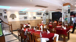 A restaurant with multiple tables set for dining, wooden chairs, and a staircase leading to an upper level. - Hotel Ekant (Faridabad)