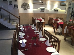 Un comedor con mesas dispuestas para una comida, con mantel rojo, servilletas blancas y copas de vino.
