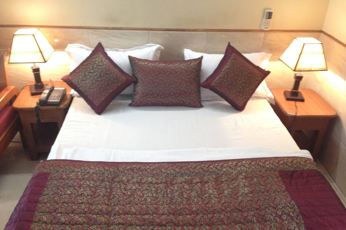 A hotel room with a bed, two bedside tables with lamps, a telephone, and patterned bedding.