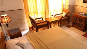 A hotel room with a bed, a desk, a chair, a small cabinet, and a TV mounted on the wall. - Hotel Ekant (Faridabad)