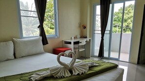 A hotel room with a bed, a desk, and a view of greenery through the windows. - Papangkorn House (Surat Thani)
