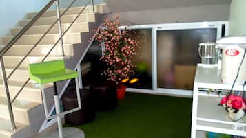 Una escalera con una silla verde, una planta en maceta con flores rosas y una cafetera blanca.