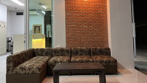 A modern living area with a sectional sofa and a small table, a brick accent wall, and a hanging light fixture. - Papangkorn House (Surat Thani)