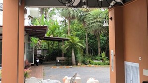 An outdoor seating area with tables and chairs, a decorative ceiling light fixture, and a view of a garden with palm trees. - Papangkorn House (Surat Thani)