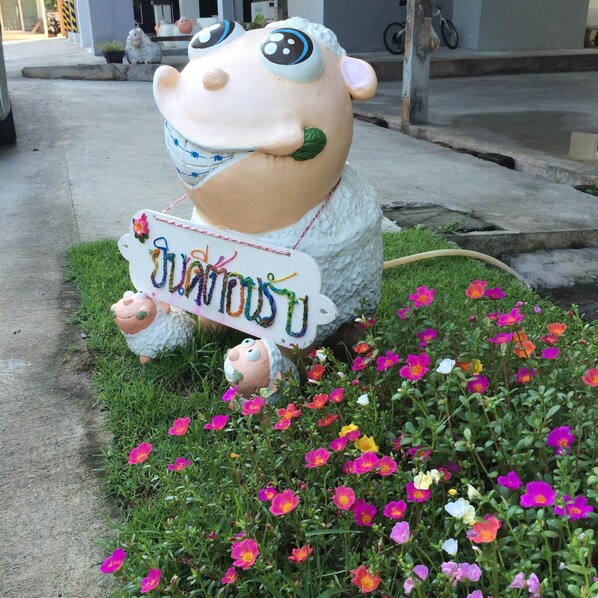 A sculpture of a smiling cow holding a sign with Thai text, surrounded by colorful flowers. - Papangkorn House (Surat Thani)
