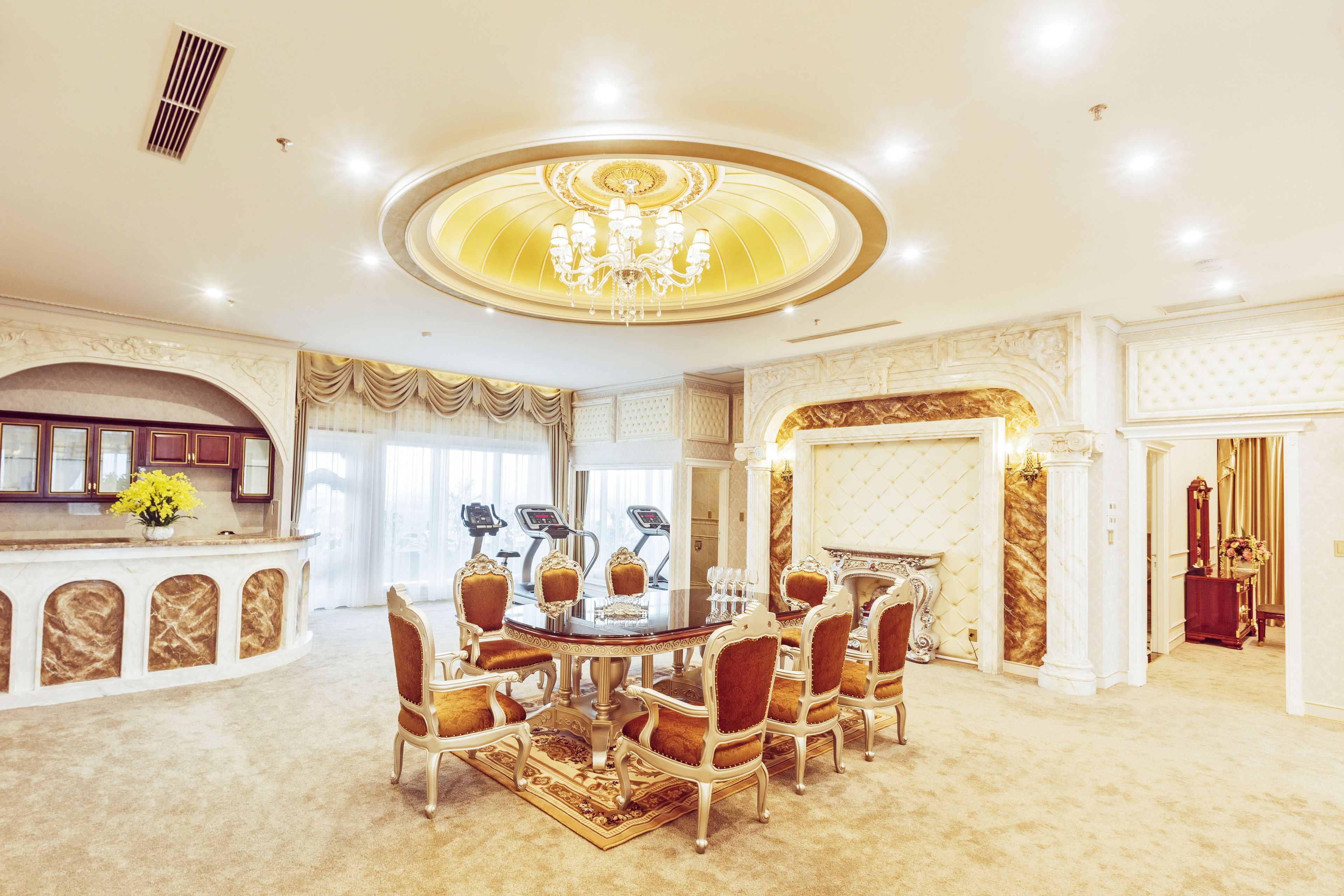 Uma sala de jantar luxuosa com uma mesa redonda, cadeiras ricamente decoradas e um lustre.