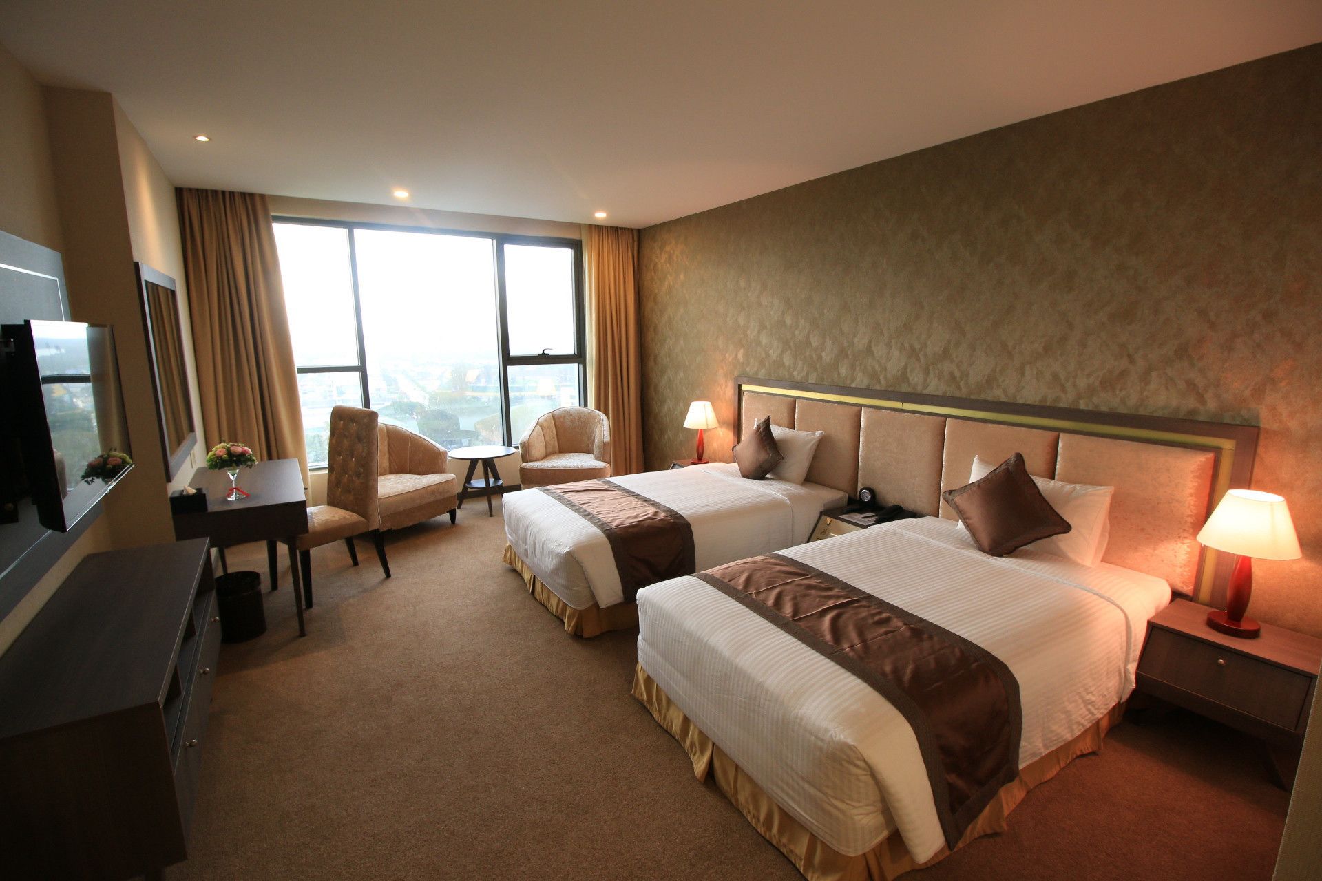 Habitación de hotel con dos camas, un escritorio, un televisor y vistas a la ciudad.