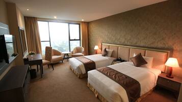 A hotel room with two beds, a desk, a TV, and a view of the city.