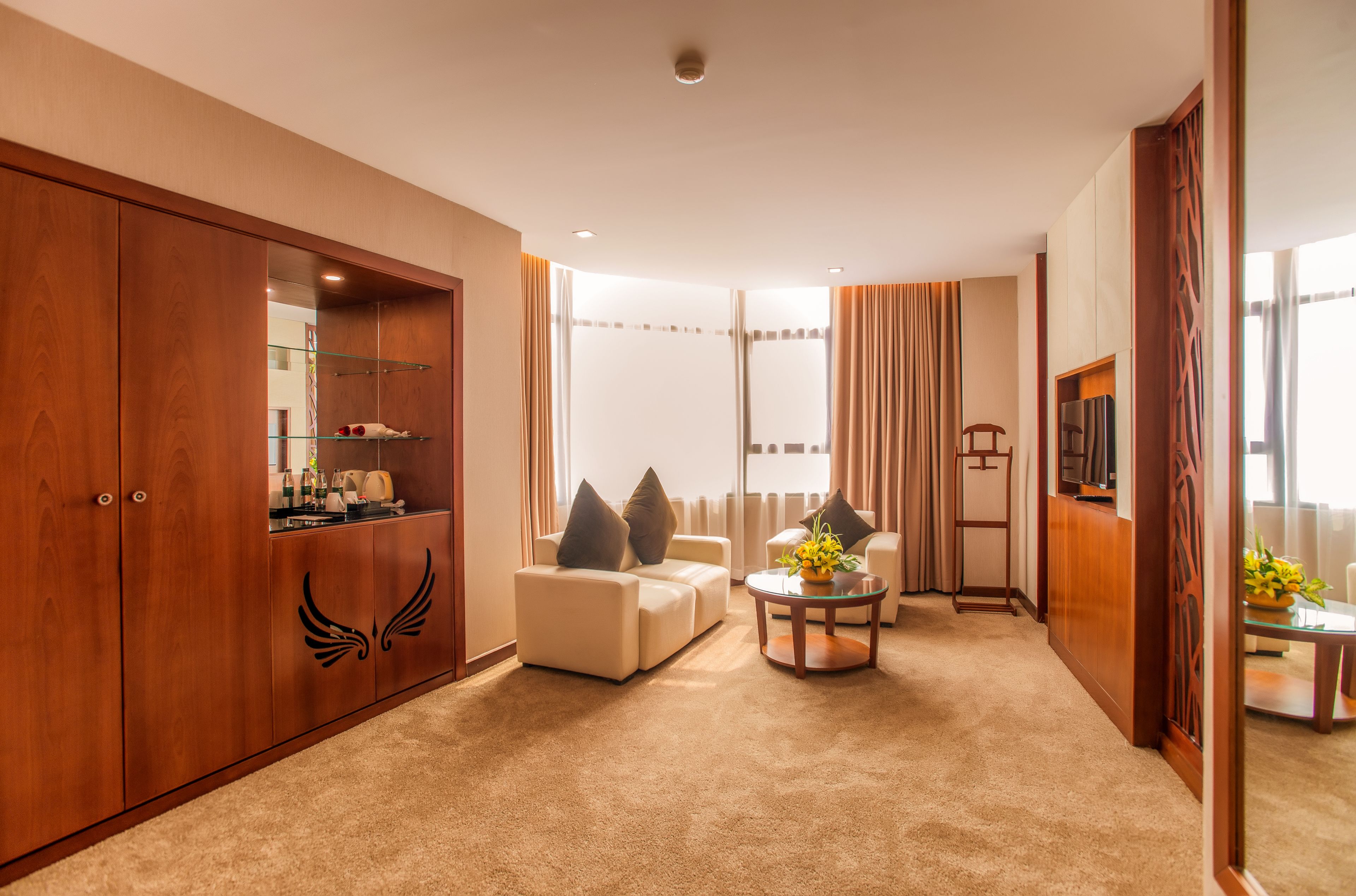 Un salón amplio con un gran armario de madera, un conjunto de sofás, una mesa de centro con flores y un televisor.