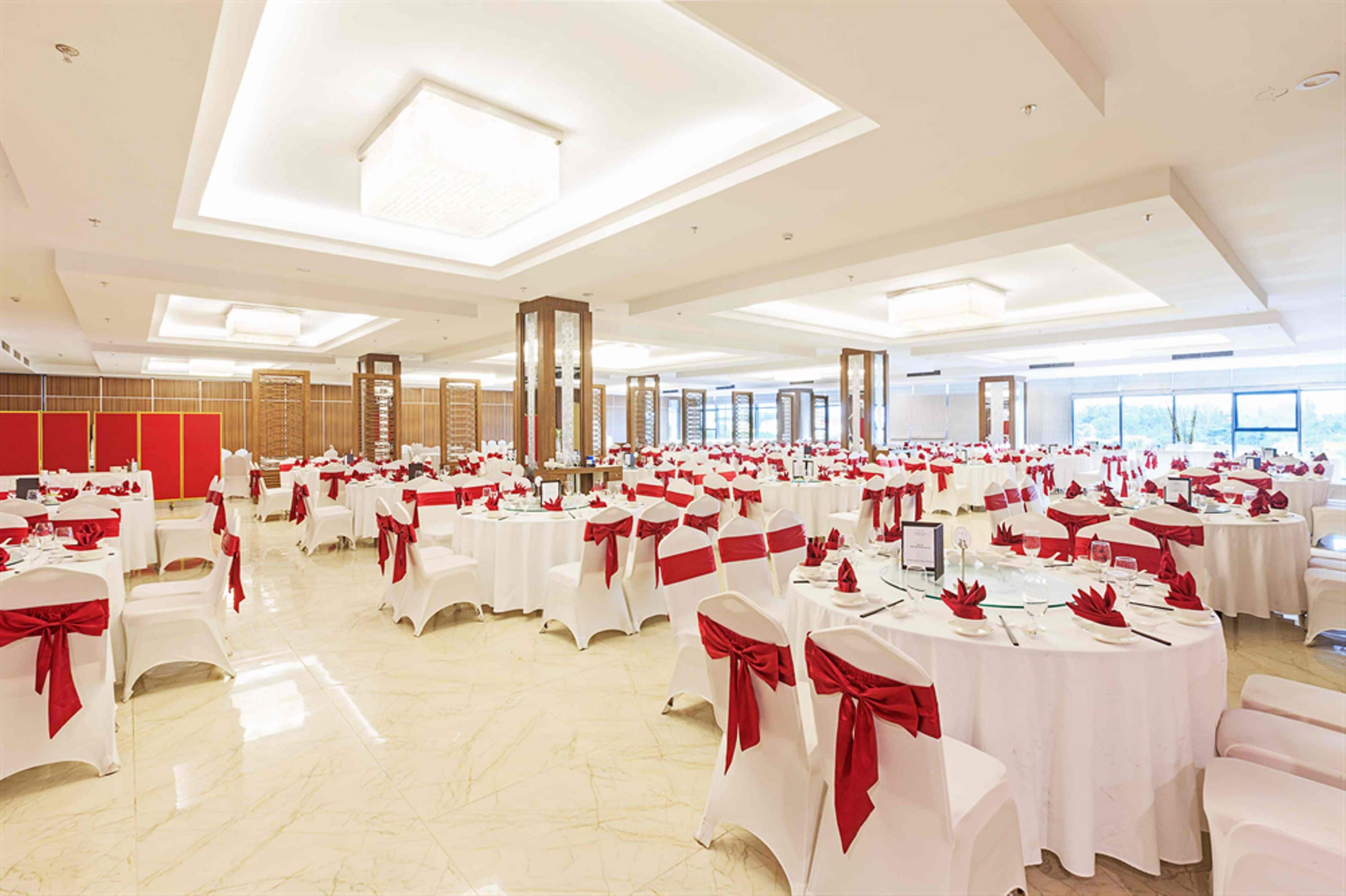 Un salón de banquetes con mesas redondas, manteles blancos y cintas rojas.