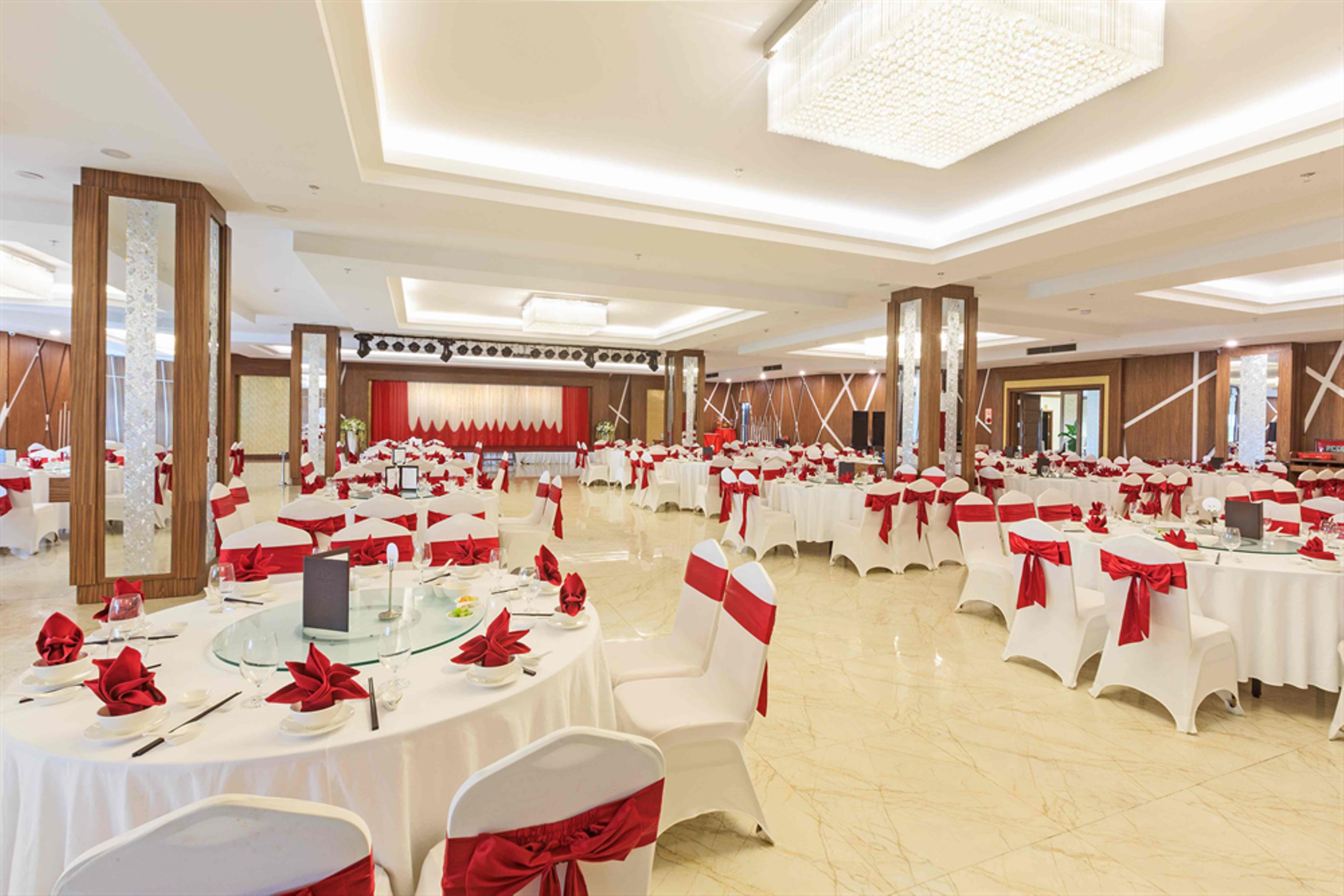 Een feestzaal met ronde tafels, witte stoelen en rode linten.